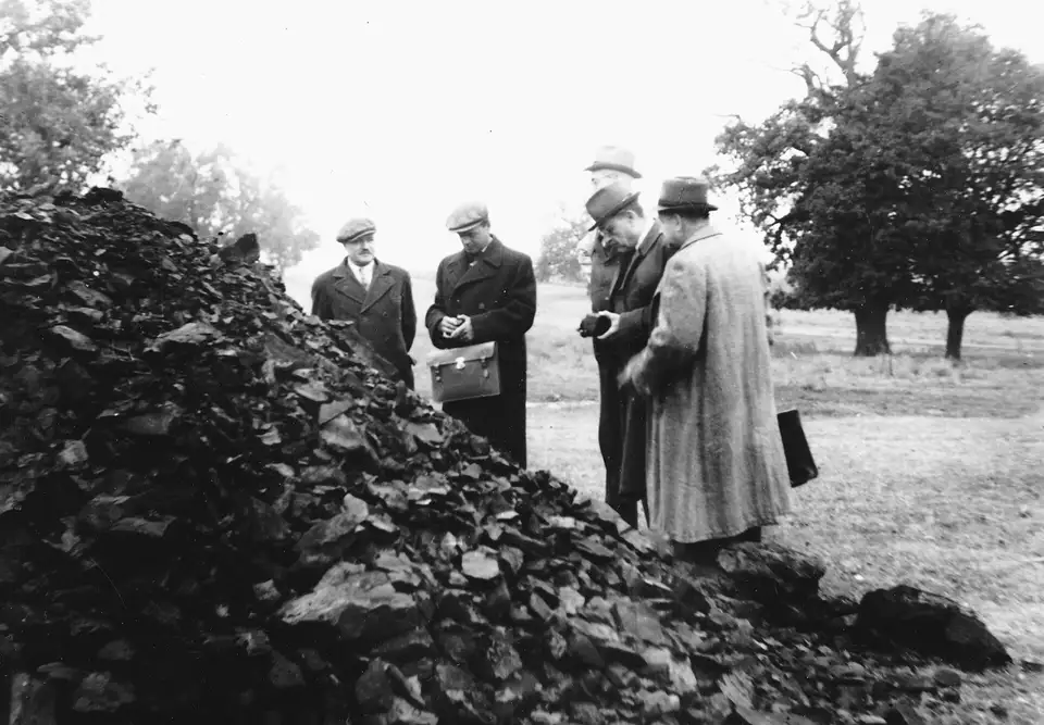 Mężczyźni w płaszczach i kapeluszach oglądają hałdę węgla